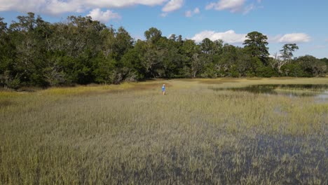 fisherman walking slowly and carefully thru the grass of wetlands in south carolina marsh during a sunny day