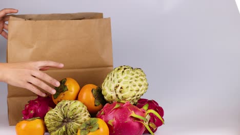 hands placing fruits into a paper bag