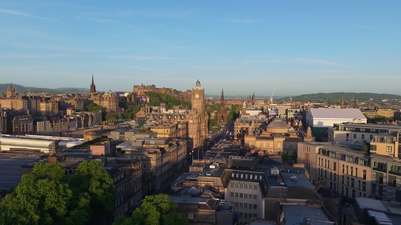 Um drone desliza sobre Edimburgo, passando pelo Monumento a Dugald Stewart e o relógio da cidade, em direção ao icónico castelo sob um horizonte vibrante.