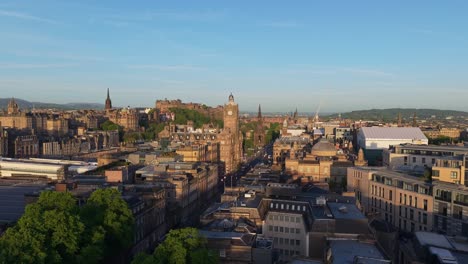 drone glides over edinburgh, passing dugald stewart monument and the city clock, heading towards the iconic castle under a vibrant skyline