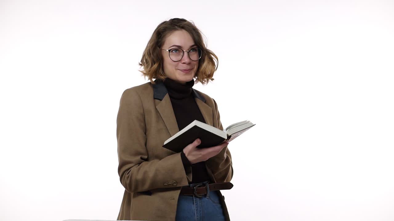 sonriente hermosa mujer joven morena con gafas y chaqueta marrón aislada sobre fondo blanco en el estudio. personas emociones sinceras, concepto de estilo de vida. lectura de libros, emocionado y sonriente pensativo
