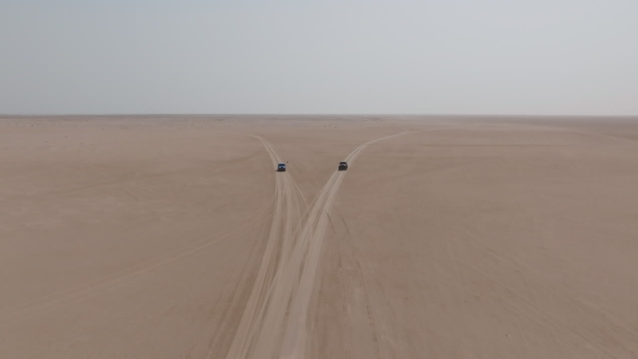 Two cars split paths on desert tracks in Bar Al Hikman, Oman, seen from above