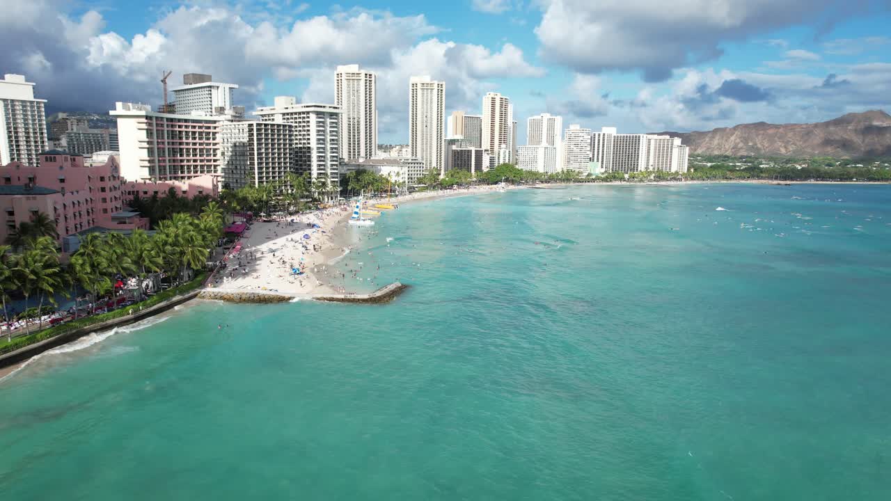 Un drone scivola lungo una spiaggia tropicale rivelando gli hotel di lusso fronte oceano e le famiglie in vacanza.