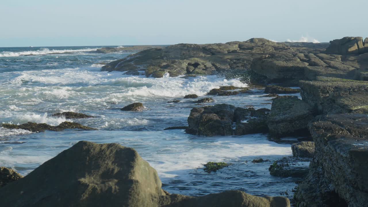 Filmato al rallentatore di potente acqua bianca che si infrange contro una costa rocciosa, creando un contrasto mozzafiato di onde spumeggianti e rocce aspre