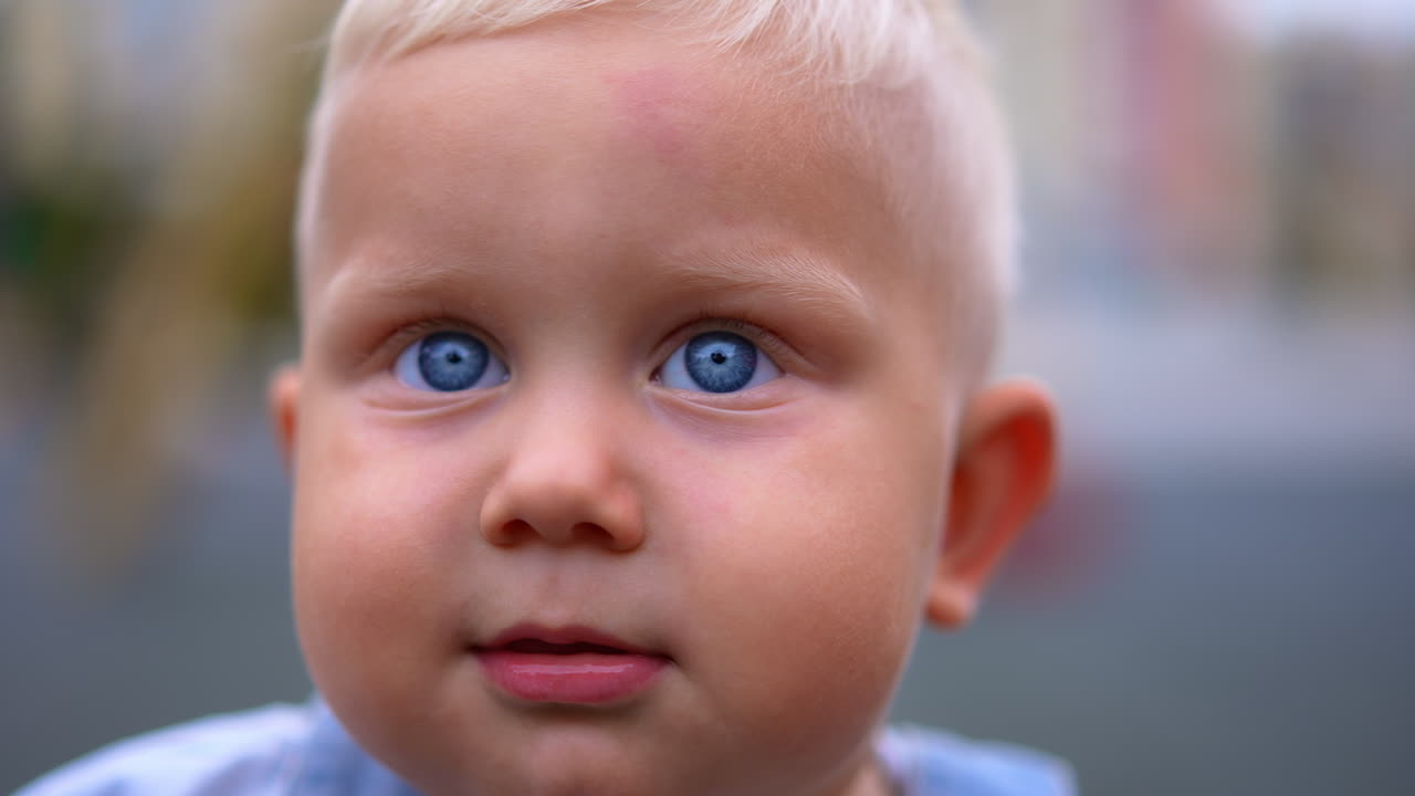 Beautiful grey-eyed Caucasian baby with fair hair. Close up. Cute smiling toddler walking outdoors.