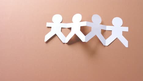 close up of people holding hands made of white paper on beige background with copy space