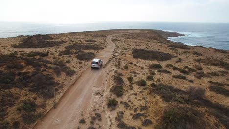 A-lone-4WD-explores-a-rocky-outcrop-by-the-ocean,-aerial-follow-shot