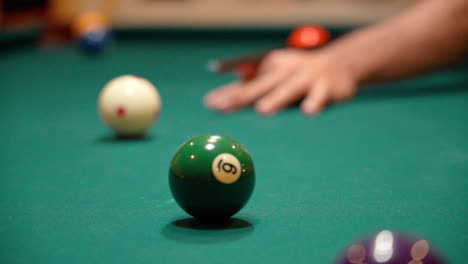 slow motion billiards person addresses and shoots cue ball on pool table with green felt using black carbon fiber cue stick then stands up close up with depth of field