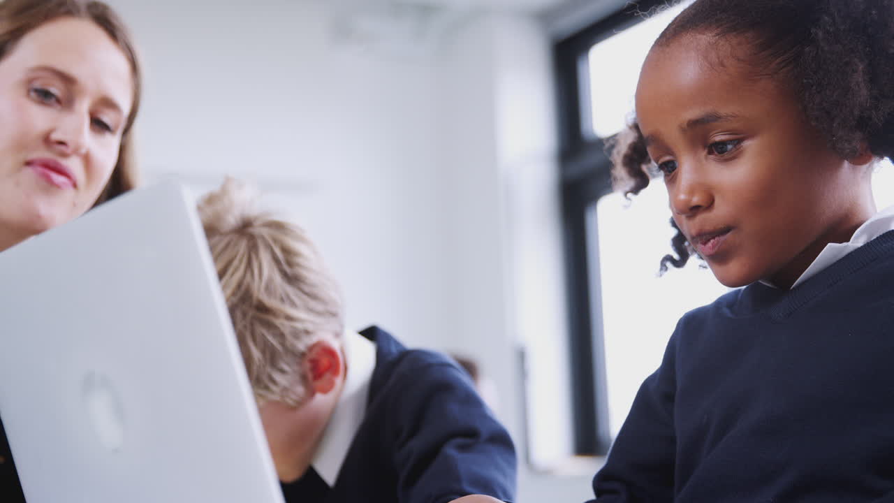 Alunna che usa un computer portatile con un ragazzo e un'insegnante in una classe di scuola primaria, primo piano