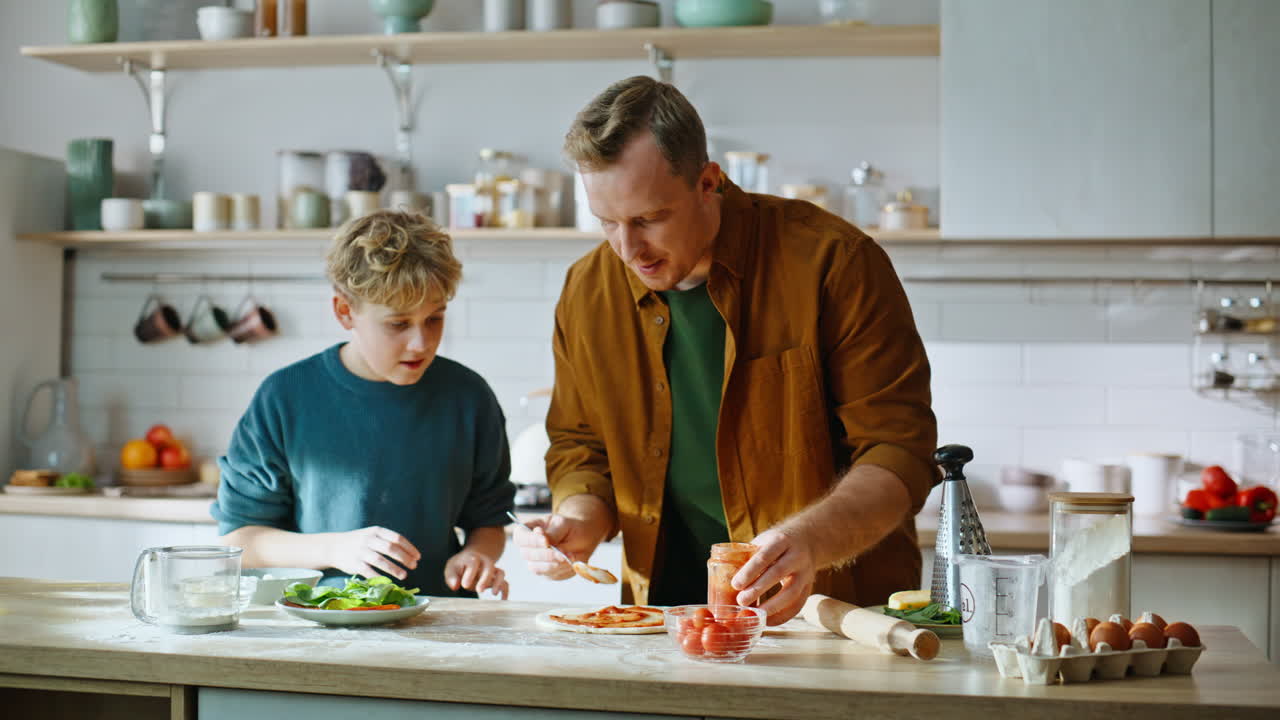 Vater bringt Sohn Pizzazubereitung bei, sie stehen zusammen in der heimischen Küche, Nahaufnahme