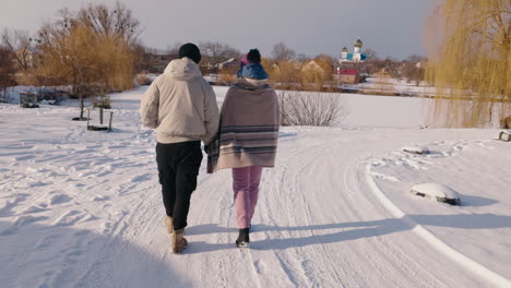 couple walking in snowy landscape near a church