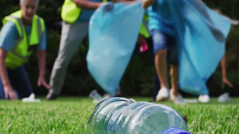 sección baja de un niño caucásico corriendo y recogiendo basura con un grupo de voluntarios en un campo