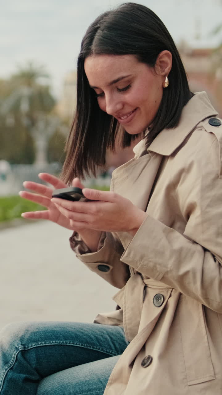 Giovane donna sorridente che usa lo smartphone mentre è seduta in un parco
