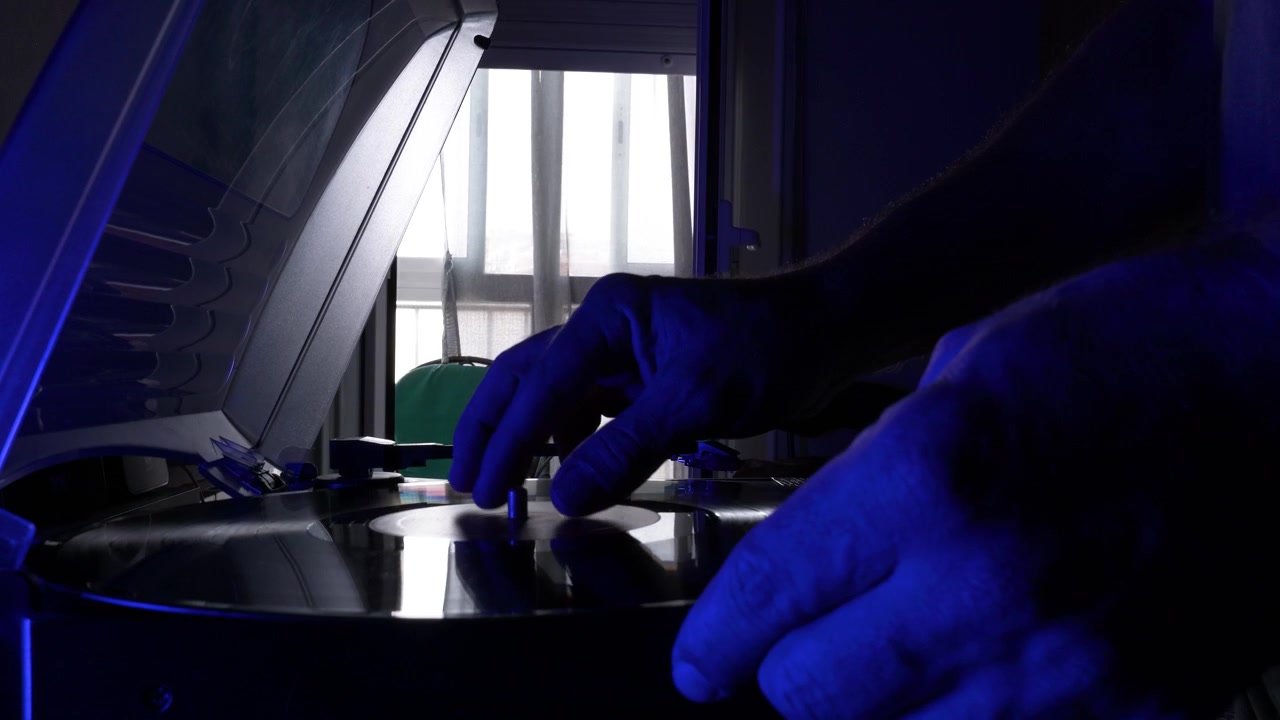 Uomo adulto che ascolta musica da un giradischi in vinile mentre usa un tablet digitale in una camera da letto accogliente con luce naturale dalla finestra. Stile di vita, relax e tecnologia a casa