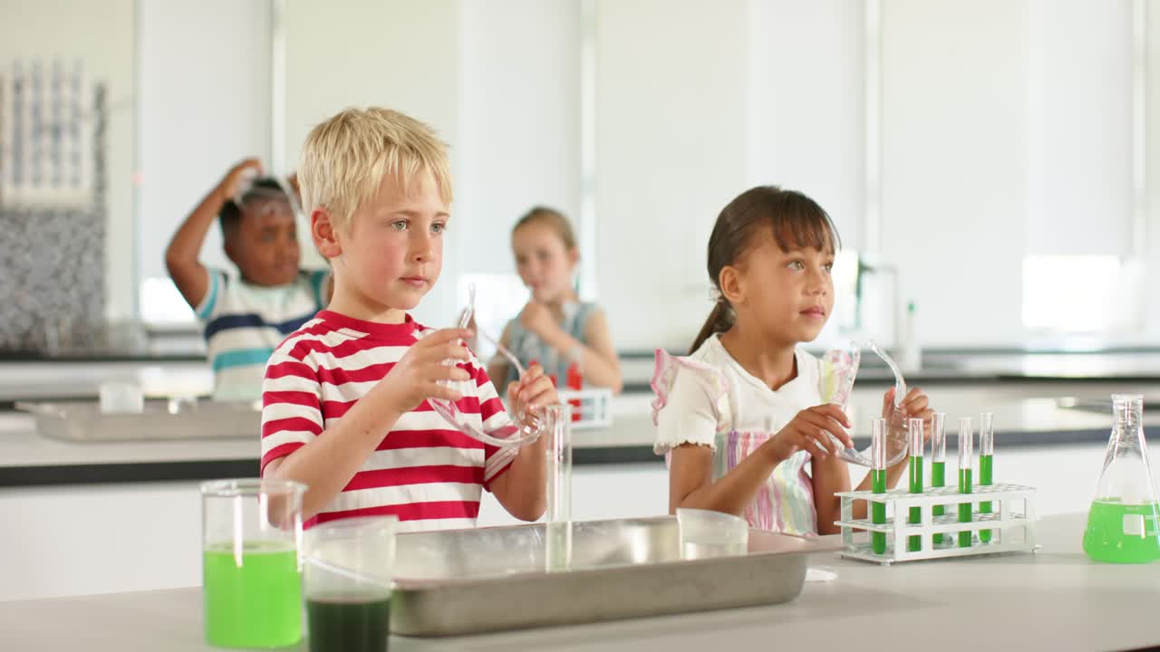 Diversi bambini delle scuole elementari si chinano per ispezionare una provetta, maneggiano provette verdi e indossano occhiali protettivi in laboratorio.