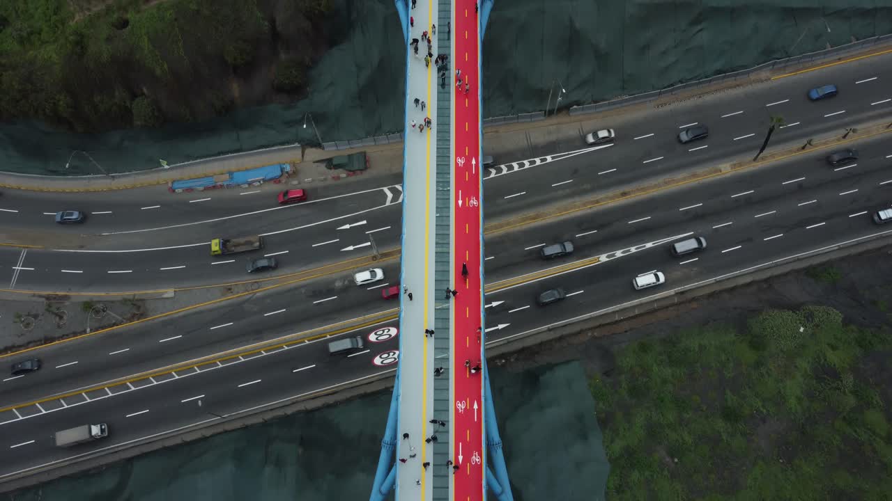 Aerial shot of new bridge built above a 4 lane street in Lima, Peru which connects two districts of Barranco and Miraflores. Drone hovers topdown above at one end of the blue bridge and tilts up