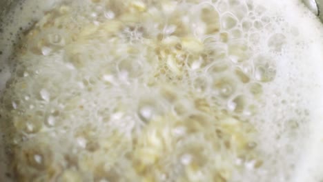 close up of oat meal boiling and bubbling in spirals in a metal sauce pan on the hob