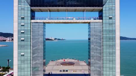 aerial dolly reverse shot of the sizable xingfu gate at xingfu park in weihai city, china overlooking the beautiful blue sea and people visiting the park on a sunny day
