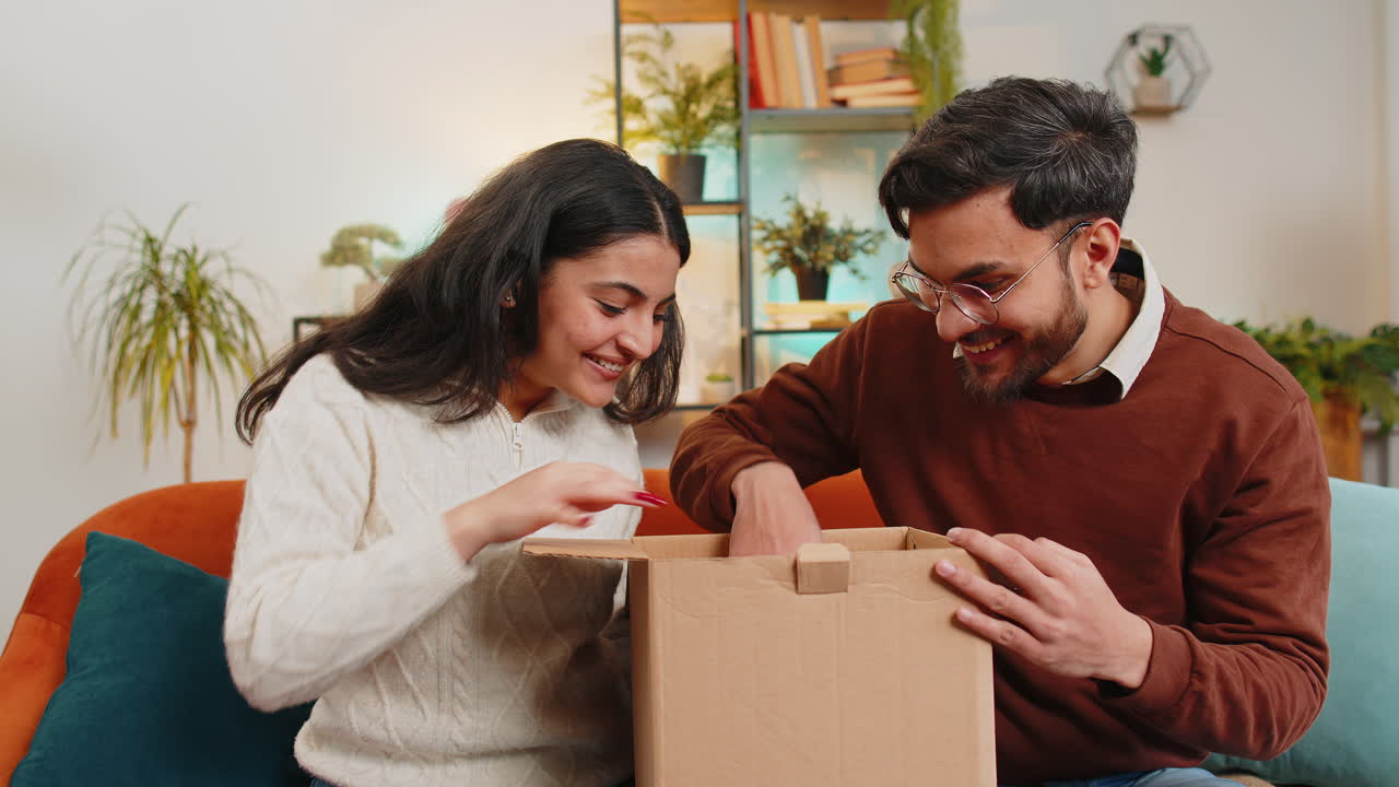una pareja feliz y emocionada abren una caja de cartón juntos, desempaquetan un buen paquete, miran adentro, compran y entregan.