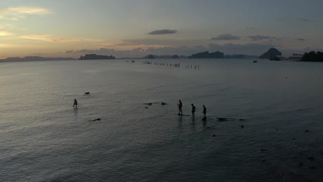 Toma-Aérea-De-La-Silueta-De-Los-Jóvenes-Pescando-En-El-Mar-De-Andaman-Poco-Profundo-Durante-La-Puesta-De-Sol,-Toma-Estática