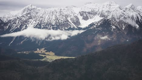 Las-Nubes-Giran-Entre-Picos-Cubiertos-De-Nieve-Y-Un-Sombrío-Valle-Sin-Nieve-Debajo.