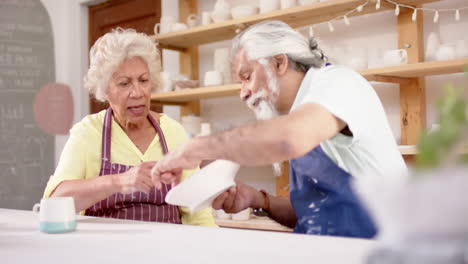 Happy-biracial-male-and-female-potters-with-plate,-discussing-in-pottery-studio,-slow-motion