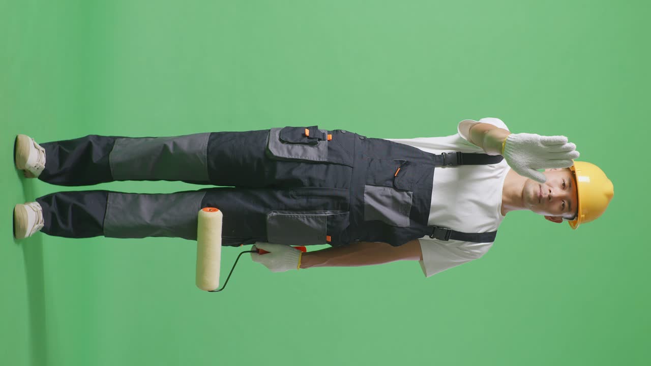 Full Body Of Asian Man Painter Wearing Safety Helmet Looking At Camera And Disapproving With No Hand Sign While Standing In The Green Screen Background Studio