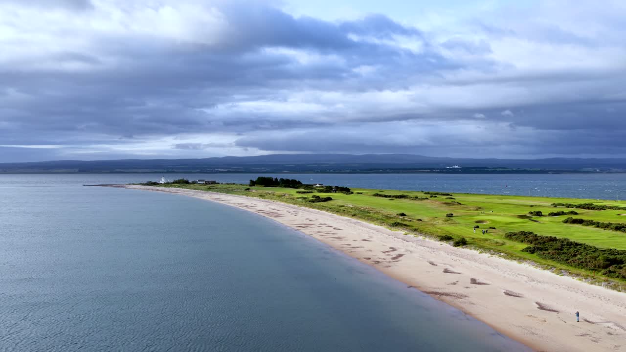 Drone glides above Rosemarkie beach, revealing coastline, green fields, and dramatic cloudy sky