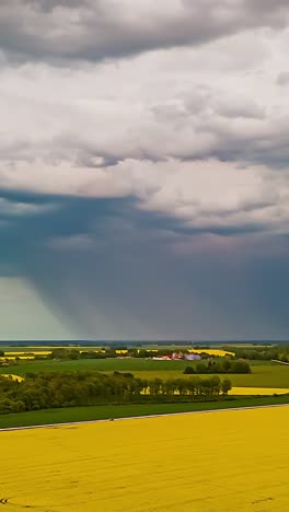 drone hyperlapse of dark storm clouds and rain above yellow rapeseed fields, vertical