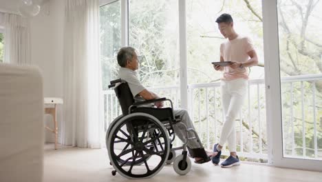 diverse male physiotherapist with tablet advising and senior man in wheelchair, in slow motion