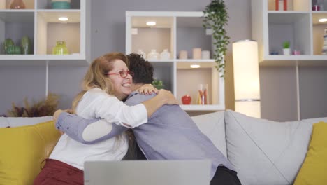 young man looking at laptop with mature mother, giving happy news, rejoicing and hugging