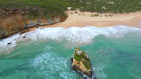 video de drone de 4k del drone volando sobre el vasto océano en el gran camino del océano, el drone se mueve hacia la playa de arena blanca donde una pareja está caminando