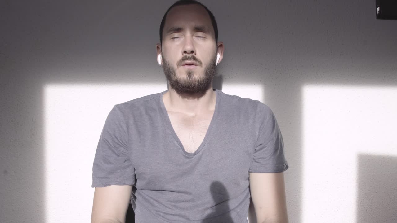 joven con barba meditando en la mañana, escuchando música tranquila, auriculares encendidos, sol brillante, tiro estático