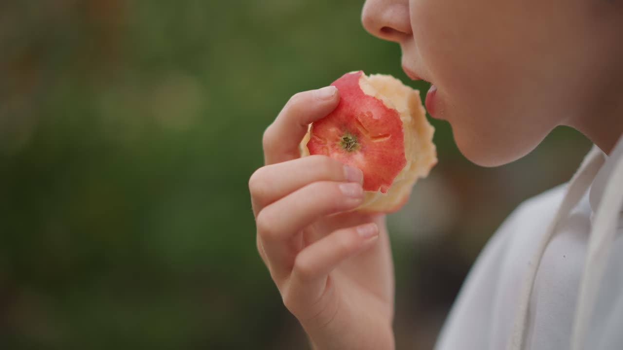 Caucasian child biting ripe apple, lively closeup of lips and hand bringing fruit to mouth backyard orchard vibe with soft bokeh, crisp flesh and audible crunch implied, young gardener and eager