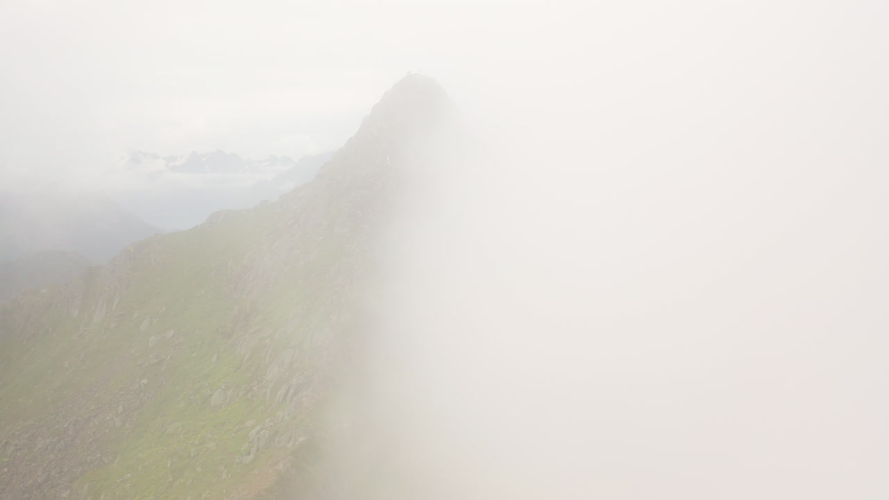 Cinematic drone shot mountain ridge with clouds on one side, Fl&oslash;ya and Djevelporten above Svolv&aelig;r in Lofoten, Norway, aerial footage