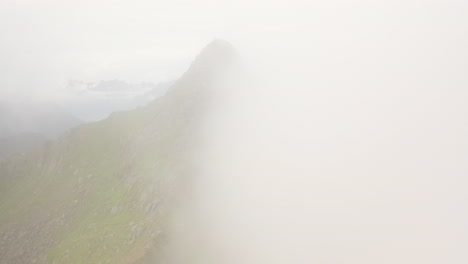 cinematic drone shot mountain ridge with clouds on one side, fløya and djevelporten above svolvær in lofoten, norway, aerial footage