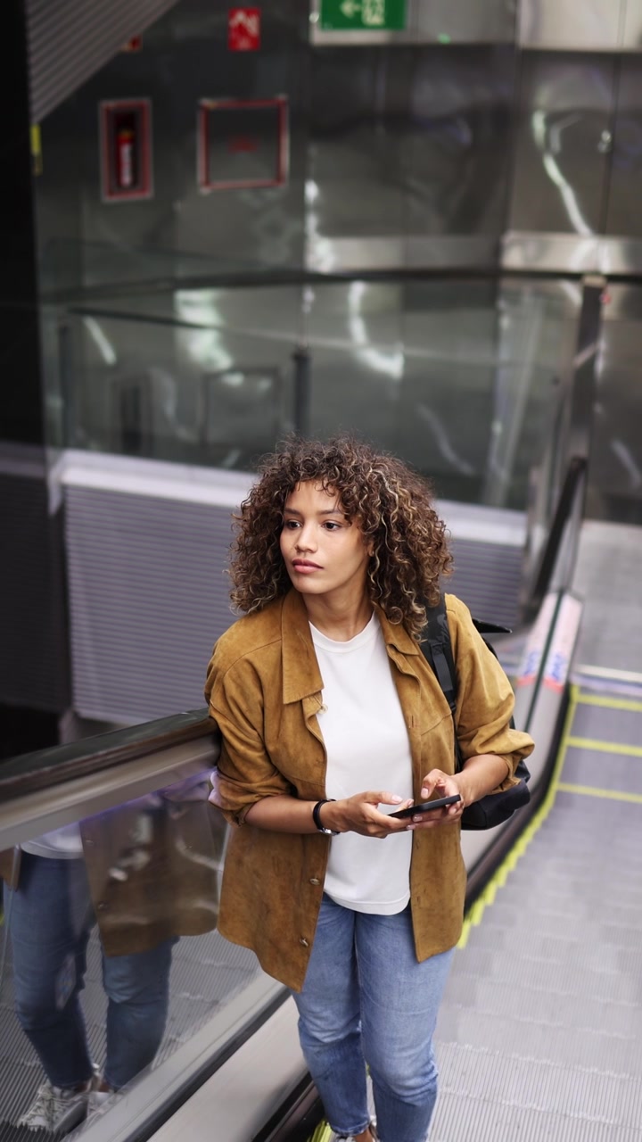 Giovane donna che usa lo smartphone mentre sale sulla scala mobile