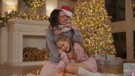 mother, little boy and girl hug next to the gifts and the christmas tree