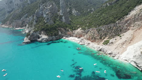 Video-Aéreo-De-Drones-Del-Paraíso-Tropical-Playa-Turquesa-Y-Acantilados-Marinos-En-El-Mediterráneo,-Cala-Goloritzè,-Con-Barcos