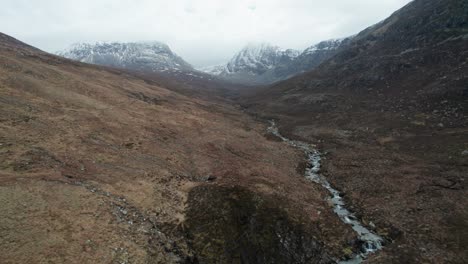 Ein-Wasserfall-Fließt-Durch-Eine-Zerklüftete-Landschaft-Mit-Schneebedeckten-Bergen-Im-Schottischen-Hochland