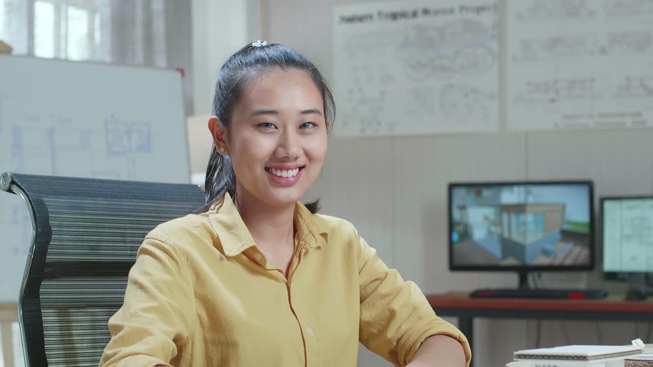 Asian Woman Engineer With Blueprint Warmly Smiling And Showing Thumb Up To Camera At The Office