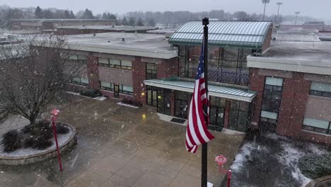 aerial orbit around american flag in front of high school building in america on snow day