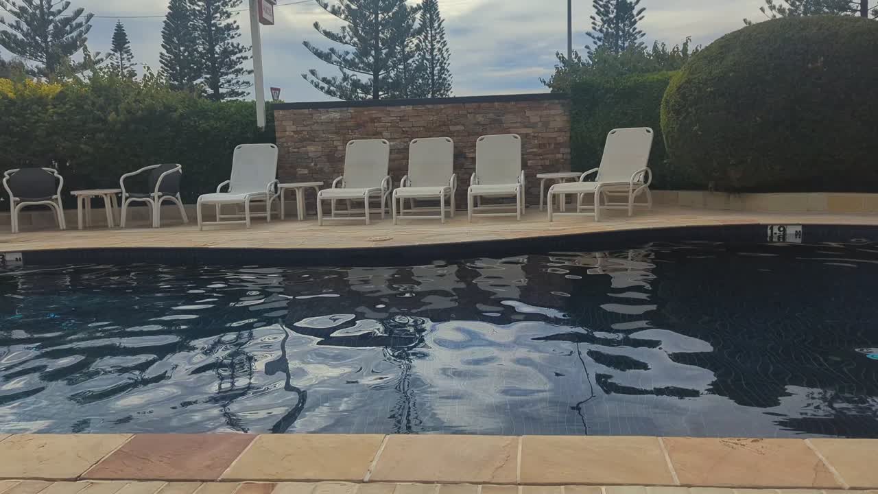 Pan left, Hotel pool area with pool chairs, garden and arbour.
