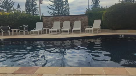 pan left, hotel pool area with pool chairs, garden and arbour.