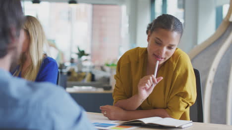 Business-Team-Having-Meeting-Sitting-Around-Table-Making-Notes-In-Modern-Open-Plan-Office