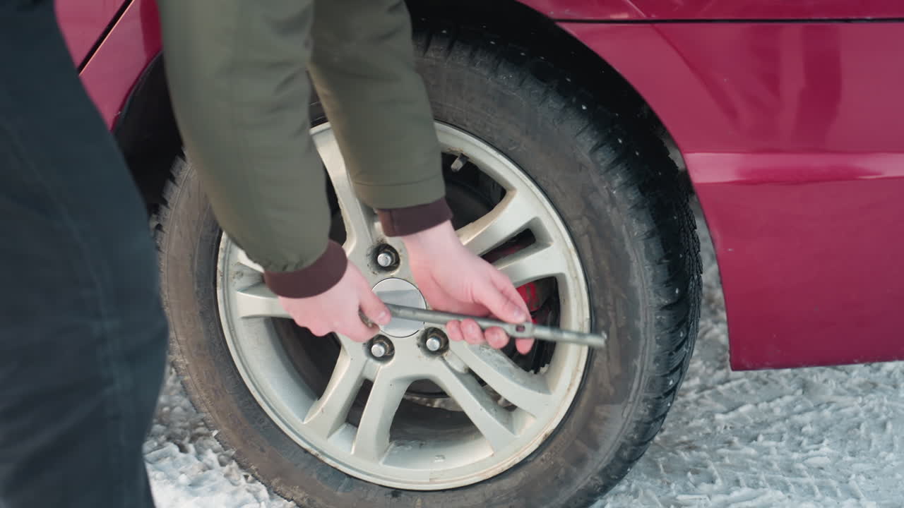 jack under car with person trying to loosen tire bolt, winter setting, mechanical work, vehicle repair, tire change, outdoor maintenance, close up on action, using spanner, snowy environment