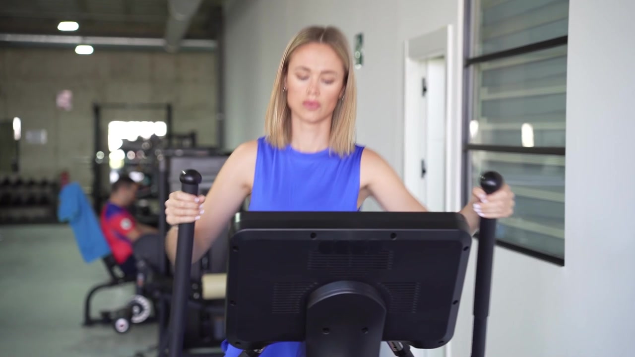 Una donna bionda si allena energicamente su una macchina ellittica in palestra, mostrando determinazione.
