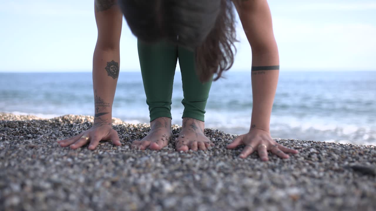Yoga instructor performing forward fold pose on pebble beach