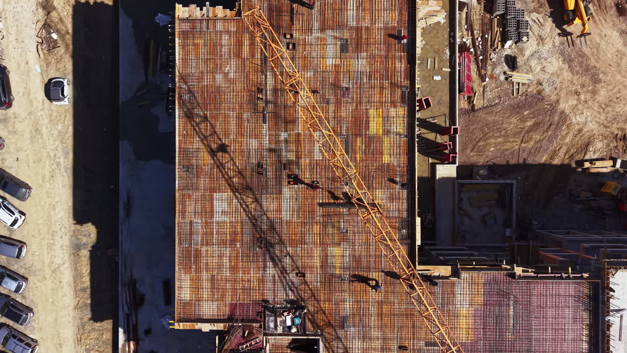 Construction site in a busy area shows workers, cranes, and building materials on a structure under development during daylight hours