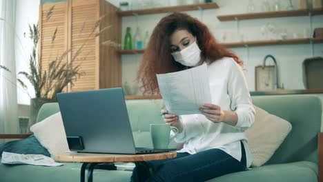 work from home during covid-19 pandemic. a woman in a face mask is working from home on quarantine
